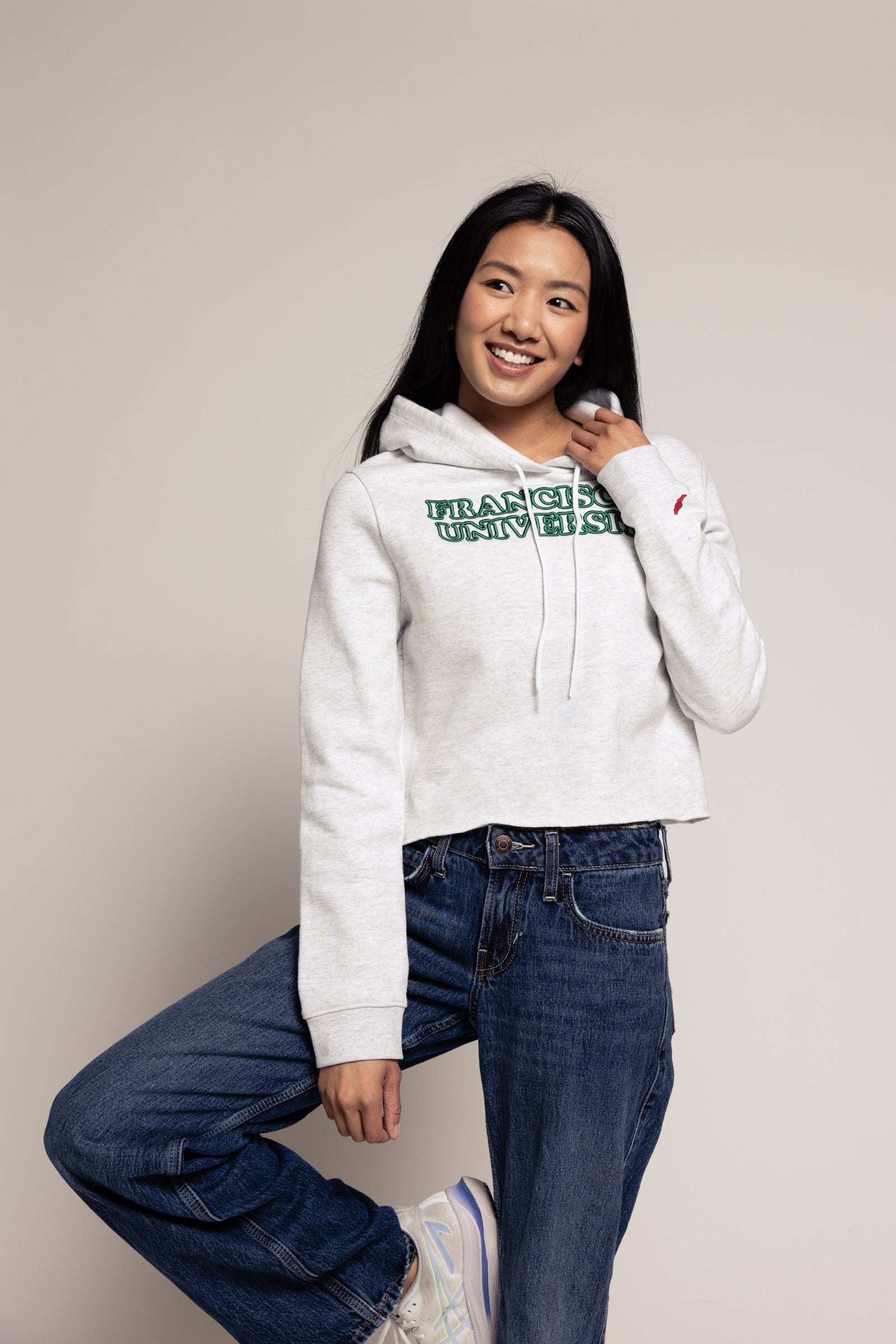 Person wearing a white hoodie with text and blue jeans on a plain background